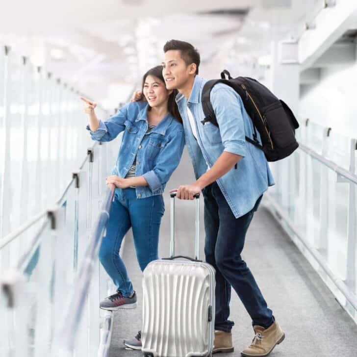 A happy couple in an airport with their luggage having fun together after reading these essential tips and advice when traveling as a couple