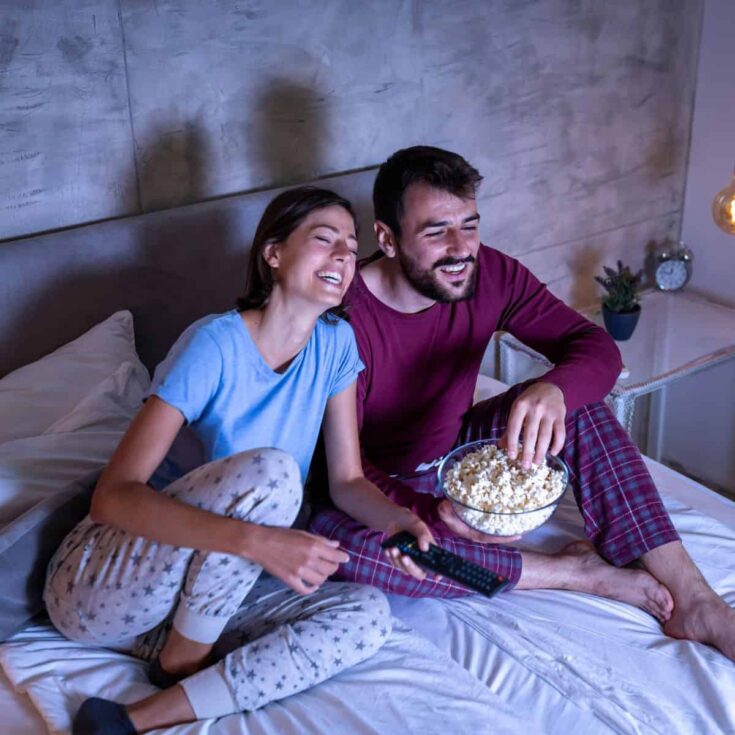A happy couple watching a movie they both love, the man holding a bowl of popcorn, after reading these date night movies