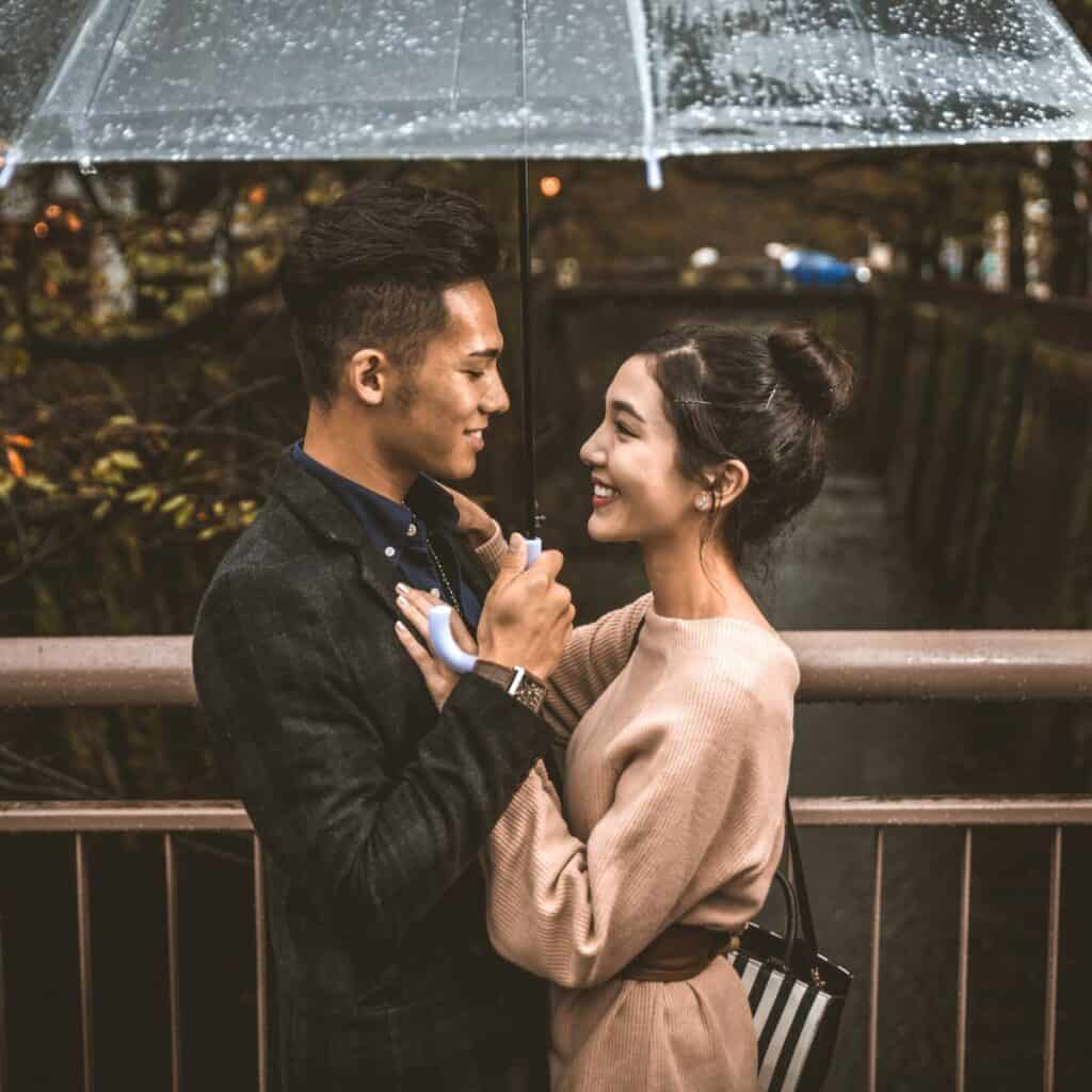 A happy couple on a rainy day under an umbrella after reading these rainy day date ideas