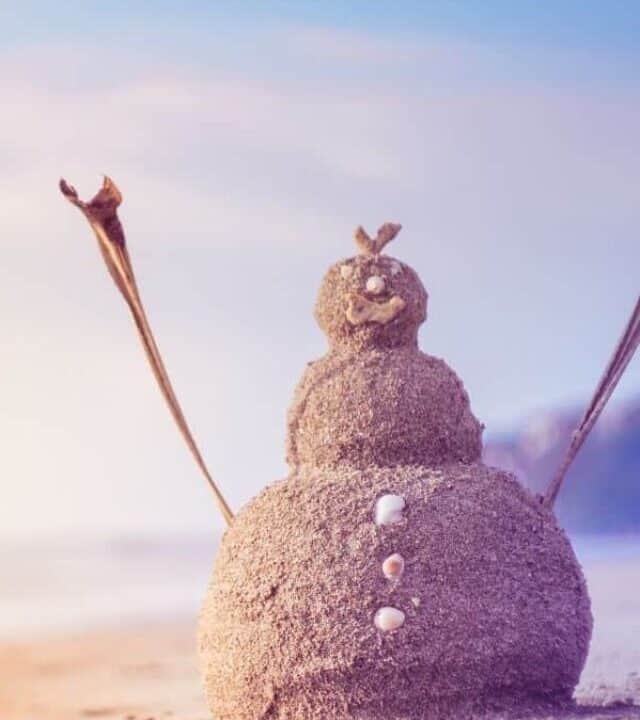 A snowman made out of sand on the beach at sunset for a Christmas in July