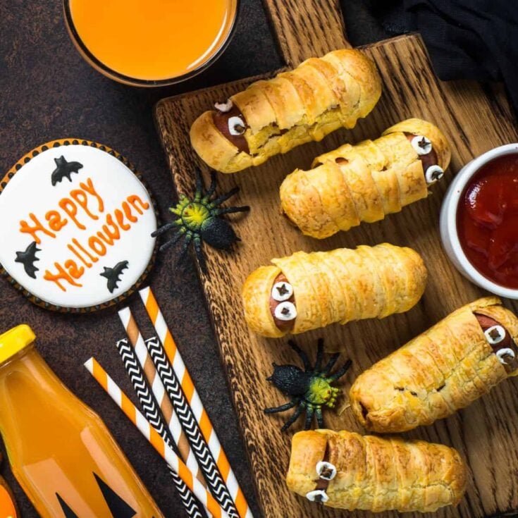 Halloween food prepared on the table including sausage mummies, gingerbread cookies, and pumpkin juice after reading these Halloween lunch ideas