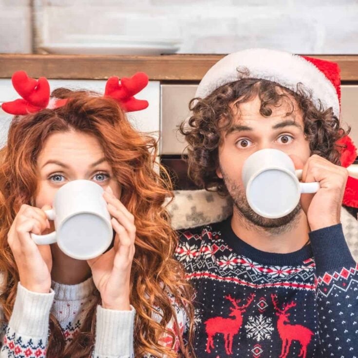 A couple drinking in a cup, the girl wearing a reindeer headband, the boy wearing a Christmas hat while asking each other Christmas questions to ask your spouse