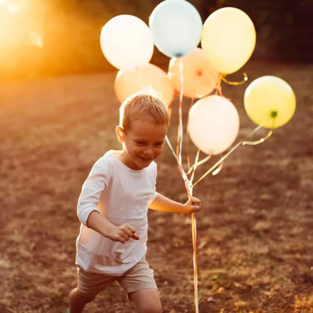 A child walking while holding a set of balloons during a beautiful sunset
