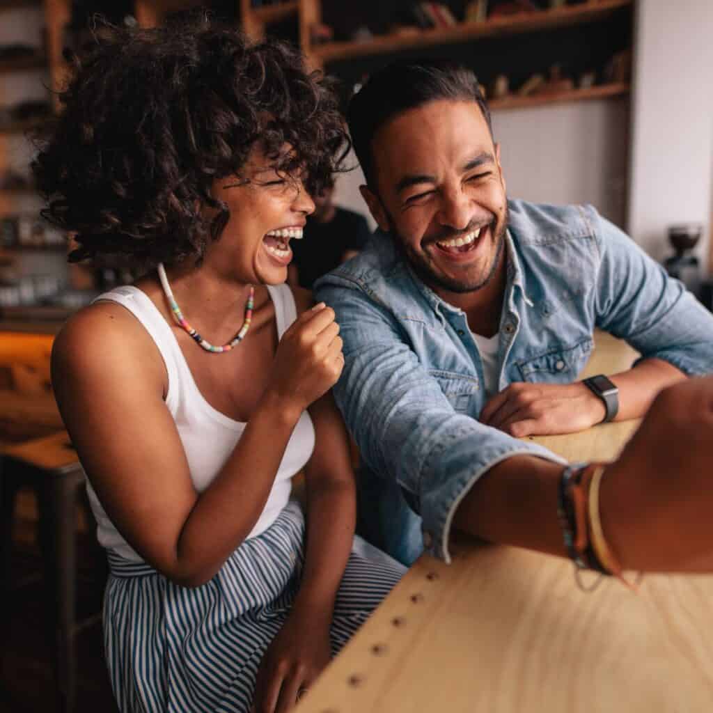 A laughing black couple at home playing Never have I ever questions for couples.