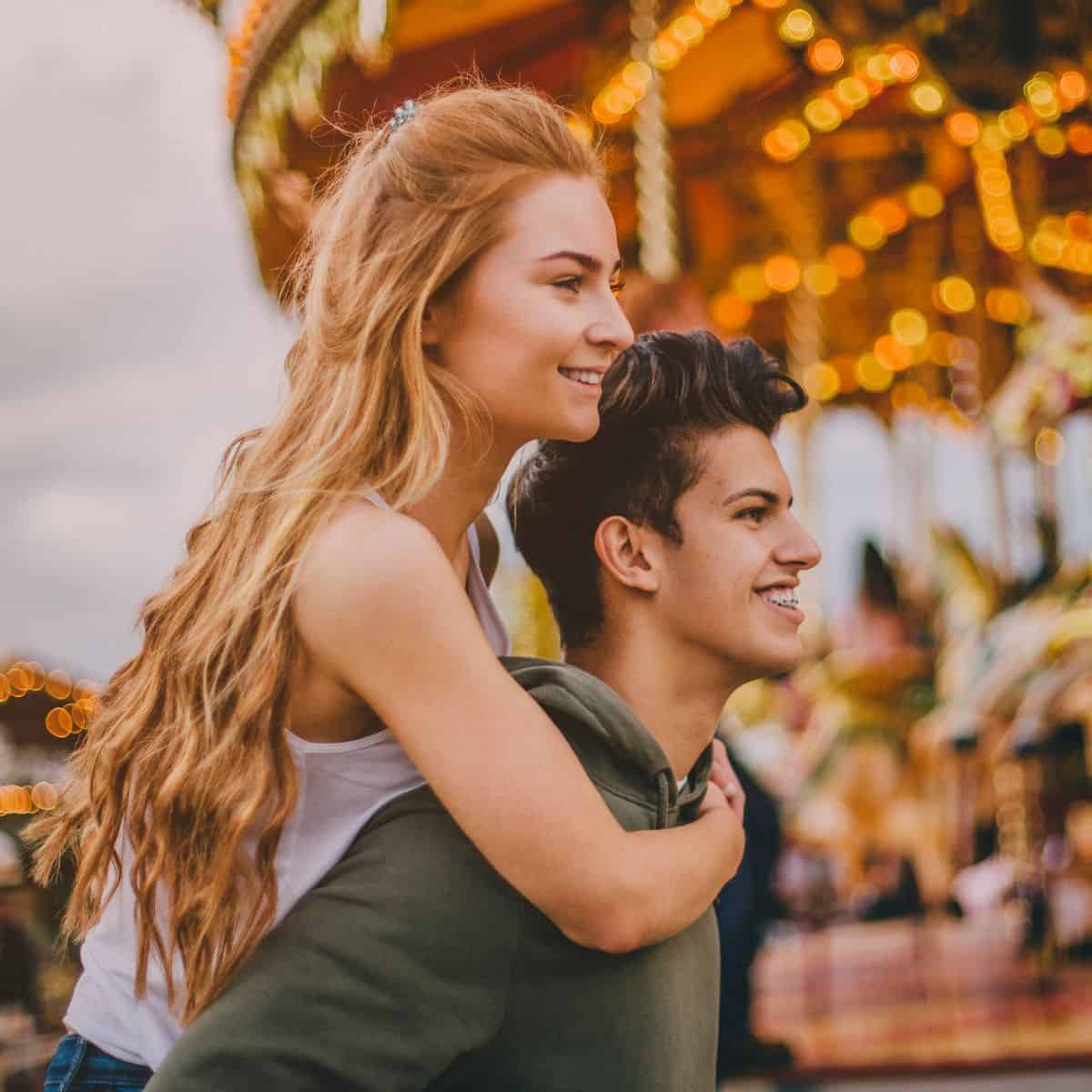 A teen couple having their first date at an amusement park, with the girlfriend getting a piggy back ride from her boyfriend