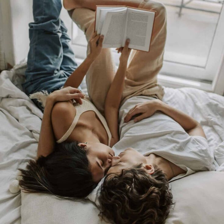 A couple reading a book while relaxing on the bed together after reading these relaxing date ideas