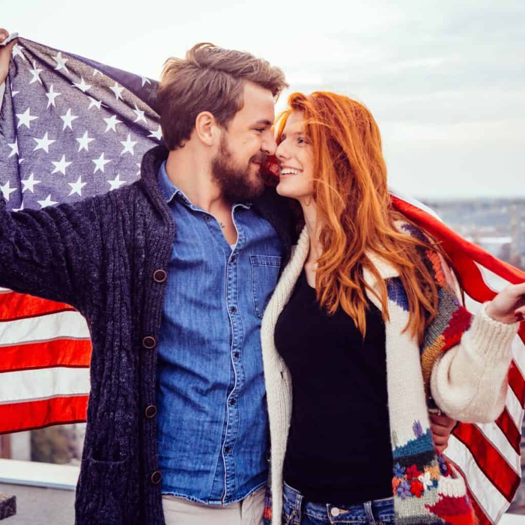 A happy couple facing each other while wrapped in American flag doing Fourth of July activities for couples