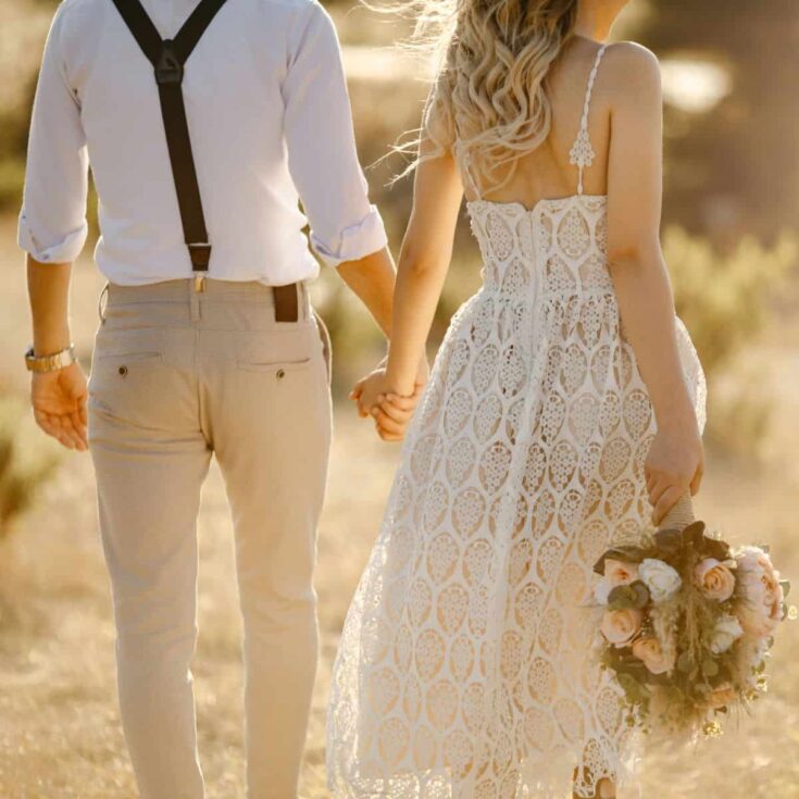 A couple on their wedding day, holding hands with their back towards the camera.