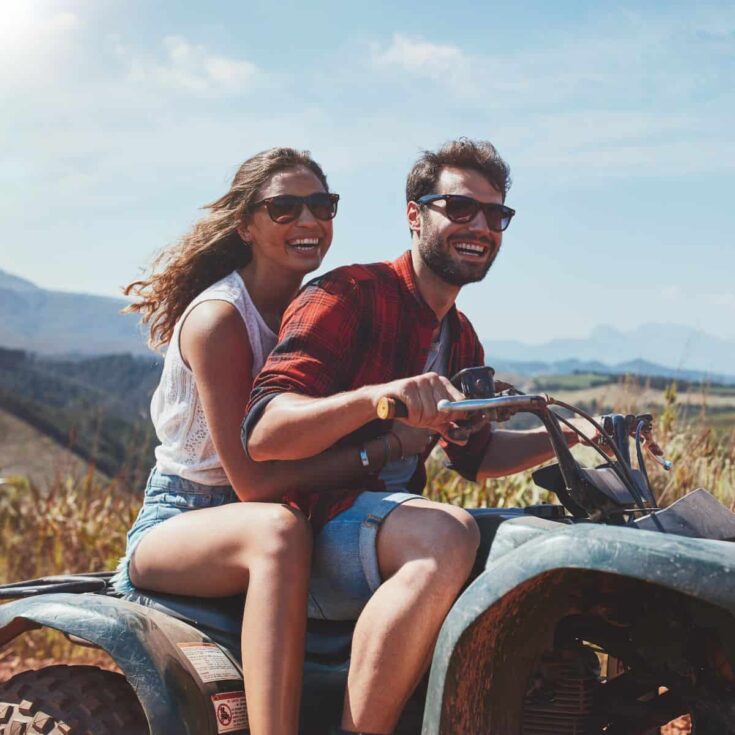 A happy couple driving a quad bike on a country road after reading these active date ideas for couples