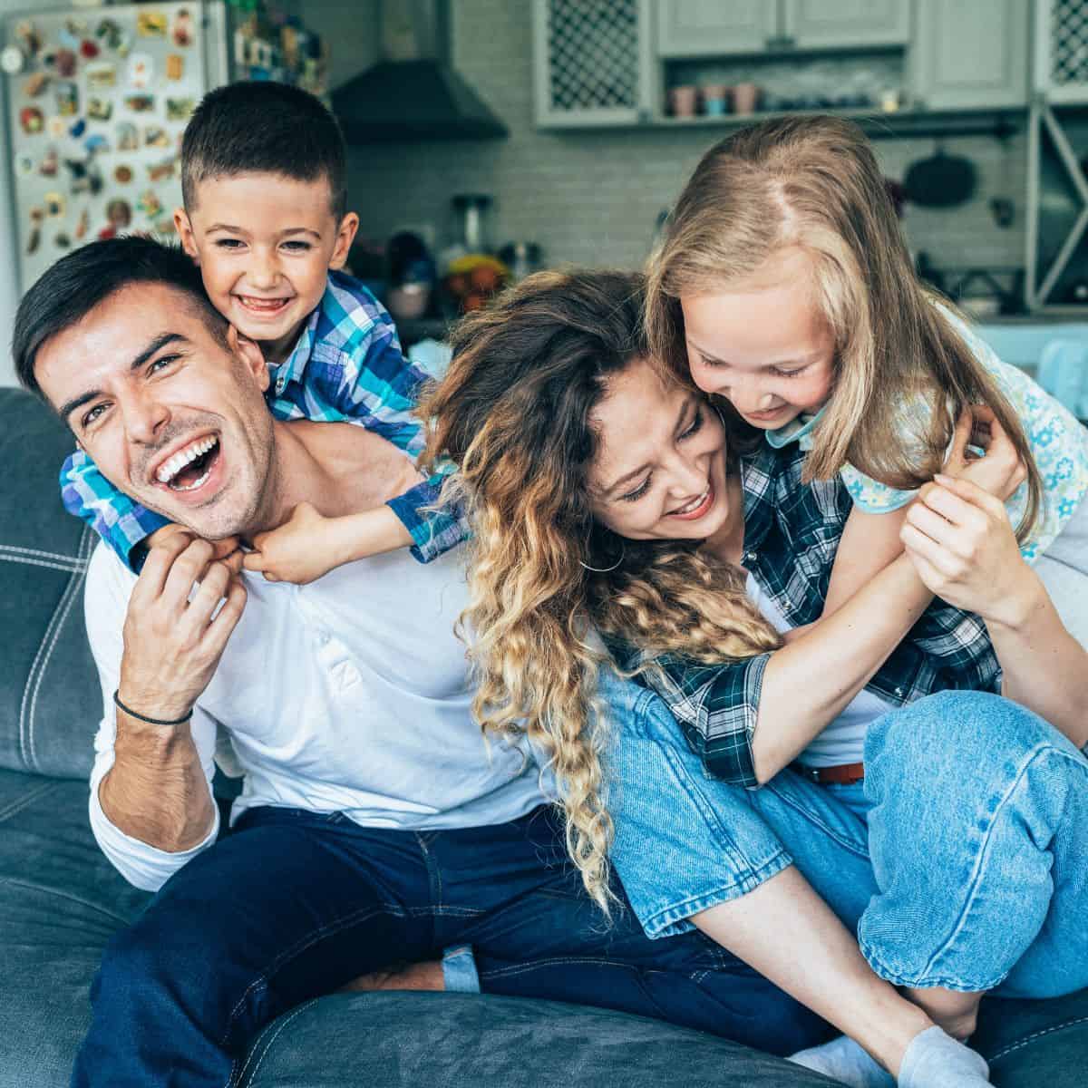 A happy family in their living room with two children hugging each their parents as they have a family fun night together