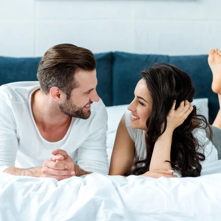 A couple on the bed, smiling at each other after finishing this 30 day marriage challenge