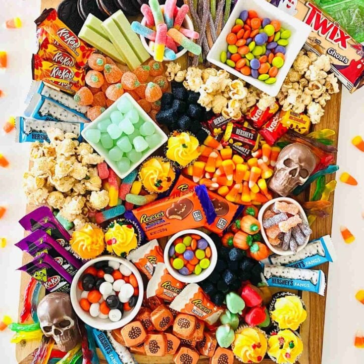 Halloween charcuterie board filled with candies, chocolates, popcorns, and more with toy skulls surrounding the board