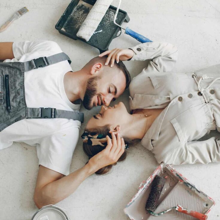 A couple laying down the floor with painting materials scattered around, after reading these creative date ideas