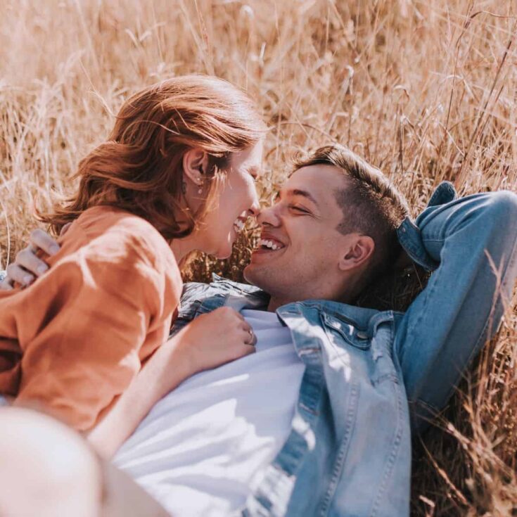 A happy couple laying down the grassy field, the girl on top of the boy saying romantic short love quotes for him
