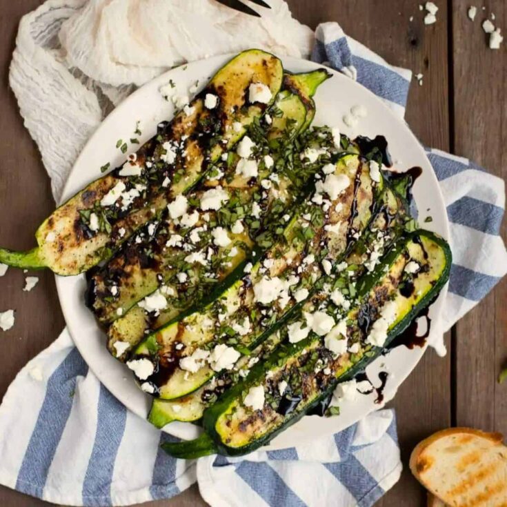 A plate of grilled zucchini with balsamic glaze, basil, and feta cookout sides