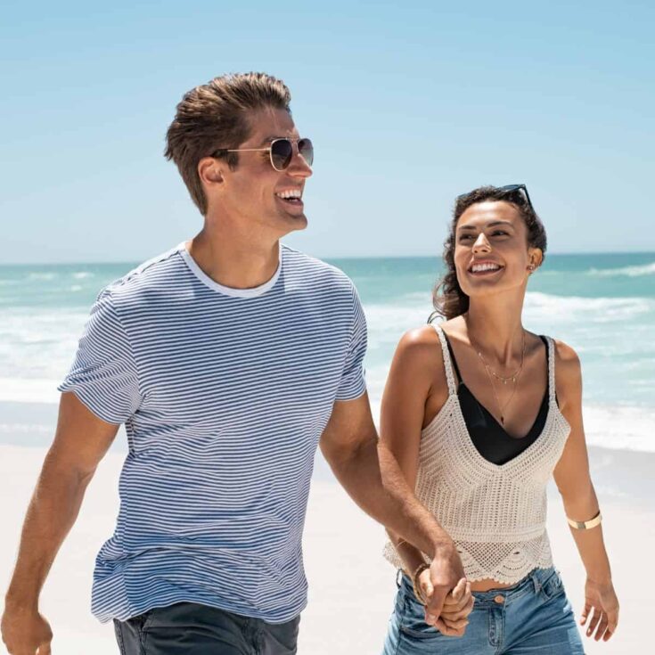 A couple walking on a beach, holding each other's hands, after reading these beach date ideas