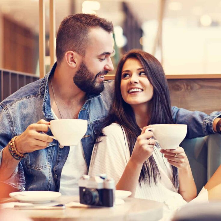 A couple at a cafe looking at each other playfully, because the woman asked these flirty questions to ask a guy