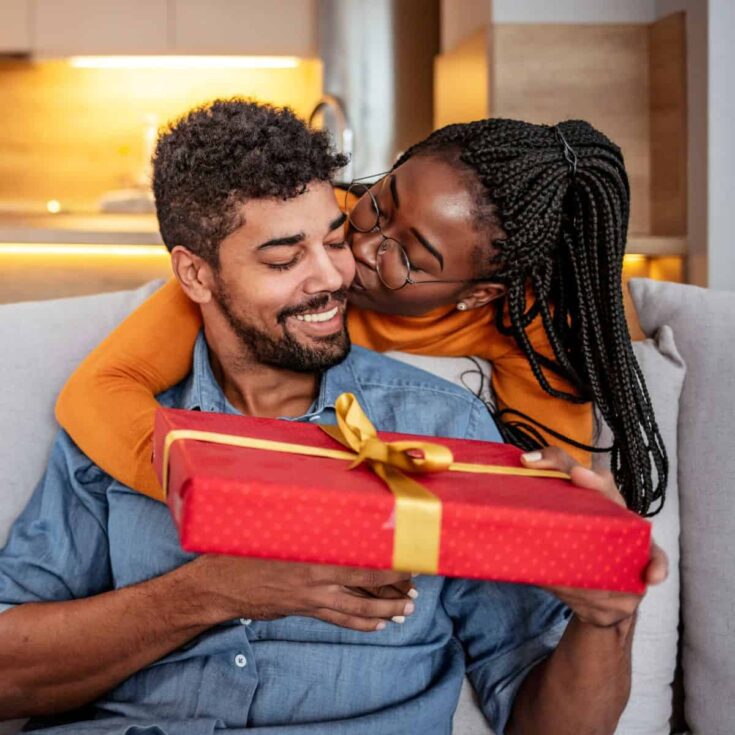 A woman kissing her man's cheeks while also giving a gift while telling one of these ways to say Happy Birthday to the love of my life