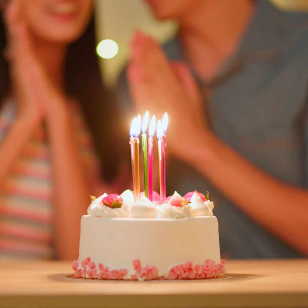 A lovely cake filled with candles, with a couple on the background: Ways to say Happy Birthday to the love of my life