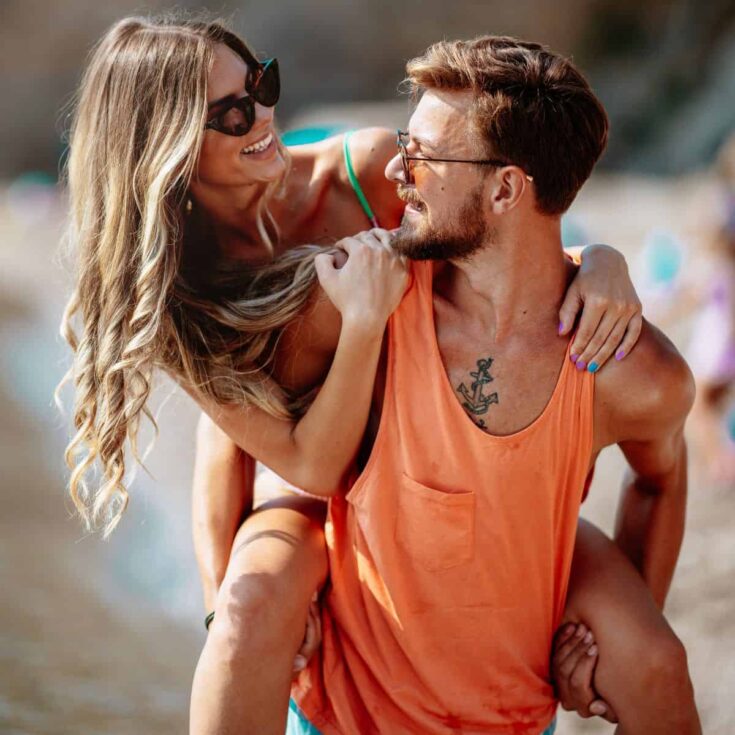A happy couple on a piggy back ride while at the beach: Summer love quotes for couples