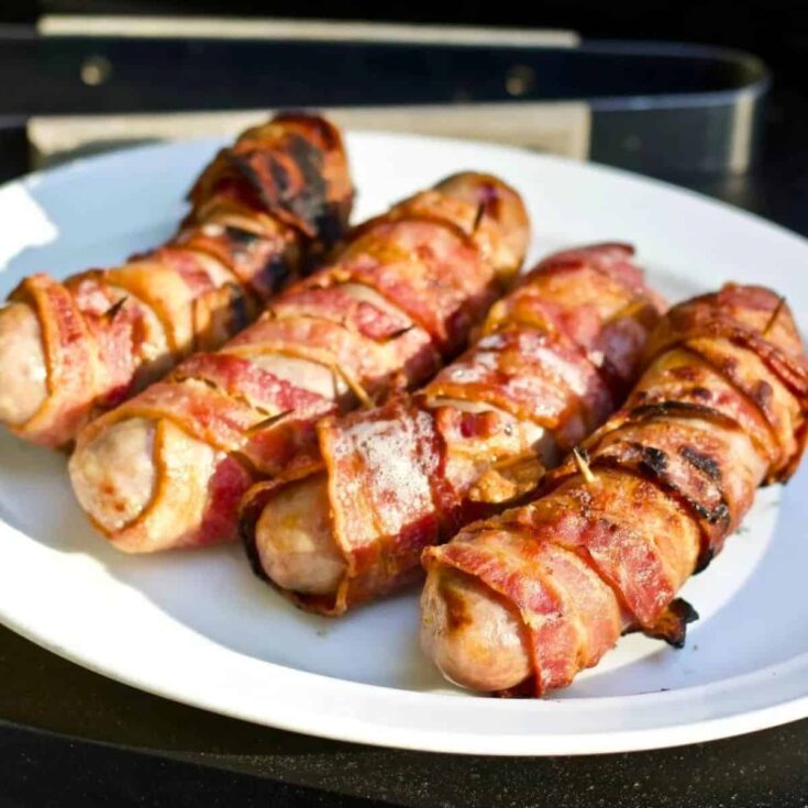 An appetizing plate of grilled bacon wrapped bratwurst cooked after reading these Summer grilling recipes