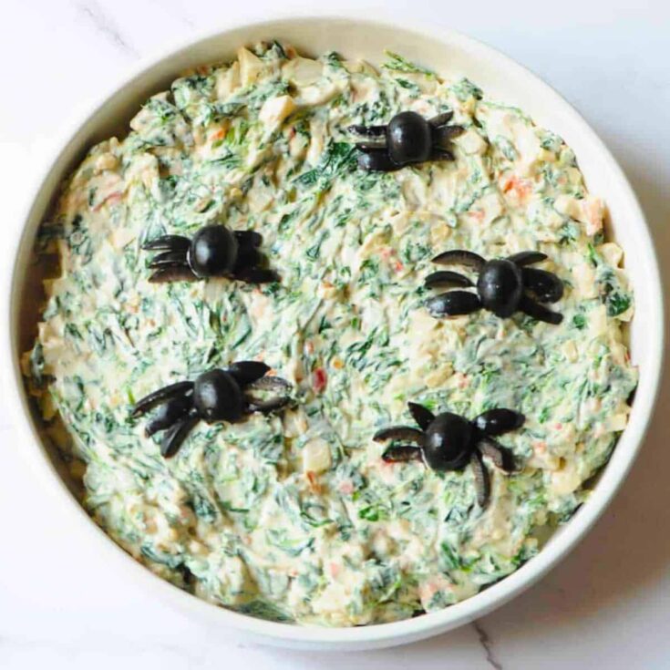 A bowl of Halloween spinach dip with spider designs cooked after reading these Halloween starters