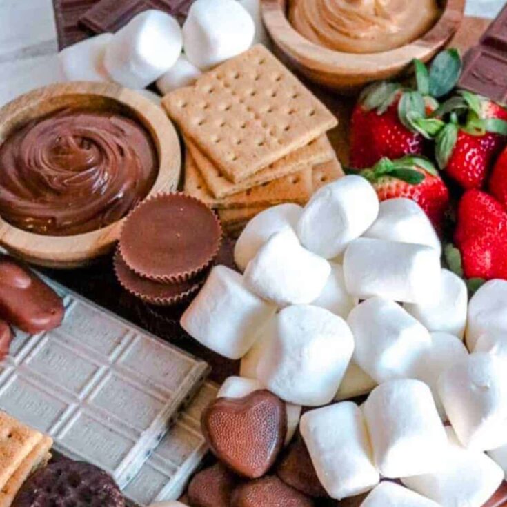 A s'mores board filled with strawberries, pretzels, marshmallows, biscuits, and more, prepared after reading these s'mores recipes