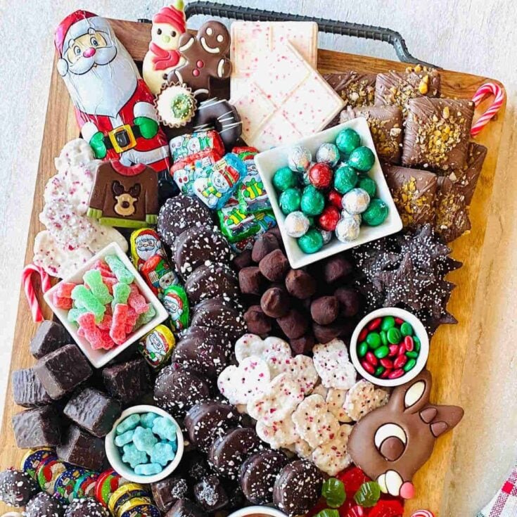 A dessert charcuterie board filled with chocolates, Santa Clause figures, snowman, candies, and more, prepared after reading these Christmas charcuterie board