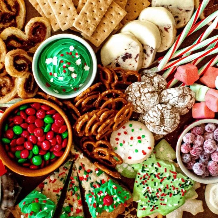 A dessert board filled with pretzels, Christmas tree cookies, marshmallows, chocolates, crinkles, and more, prepared after reading these Christmas charcuterie board