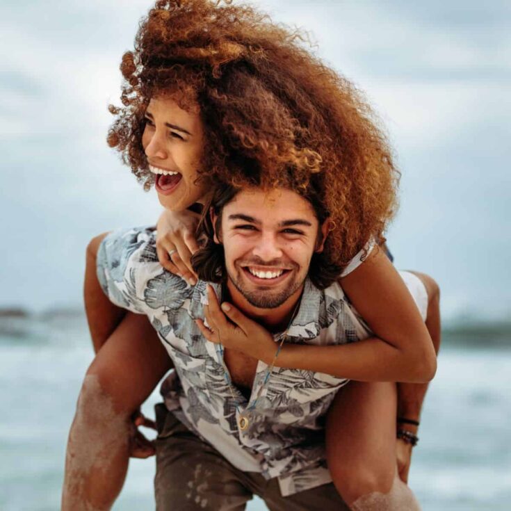 A happy couple on a piggy back ride, enjoying the beach after reading these fun date ideas