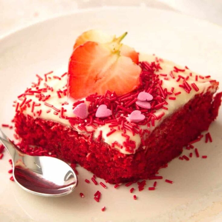 A slice of red velvet sheet cake topped with strawberry slices and some sprinkles, baked after reading these Valentines day cake recipes