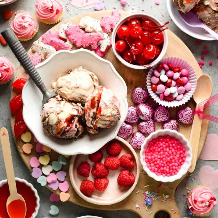 A round Valentines charcuterie board filled with ice cream, strawberries, candies, and more
