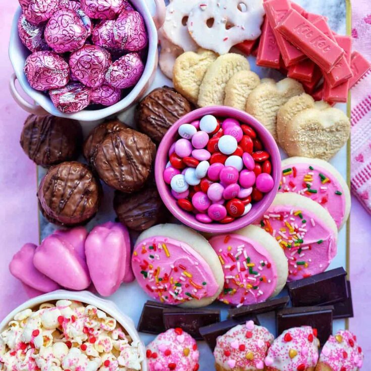 A pink Valentines charcuterie dessert board filled with chocolates, candies, cookies, and more
