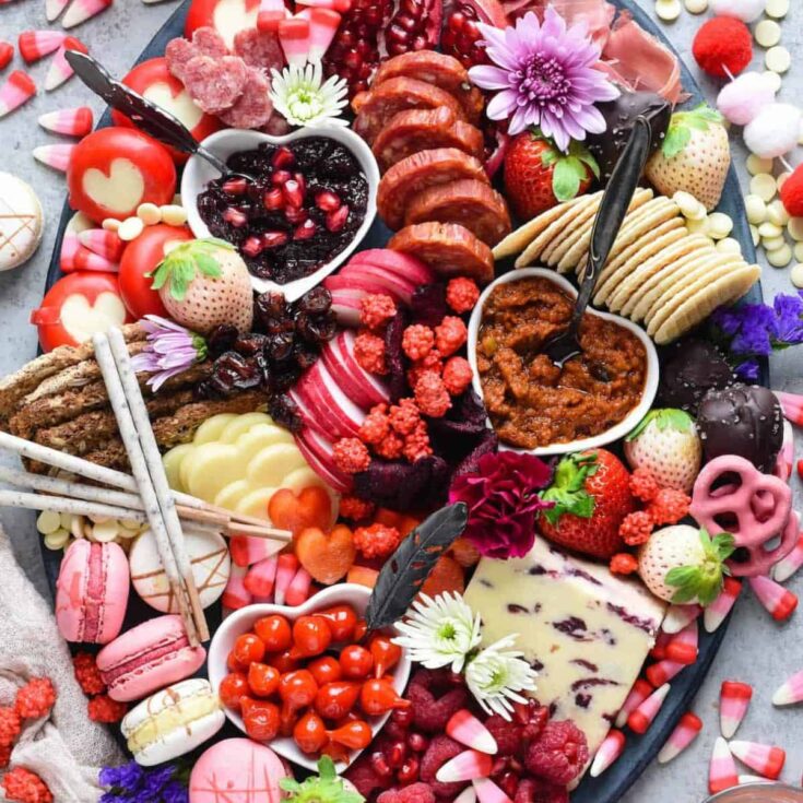 Valentines charcuterie snack board filled with apples, macarons, biscuits, cheese, and more