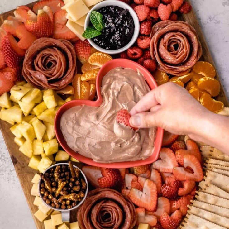Valentines day charcuterie board filled with salami roses, chocolate dip, strawberries, and more