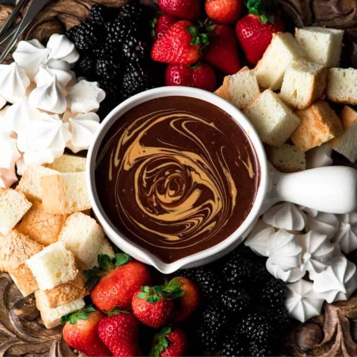 Easy chocolate peanut butter fondue surrounded by fruits, merengue, bread, and more, prepared after reading these Easy fondue recipes