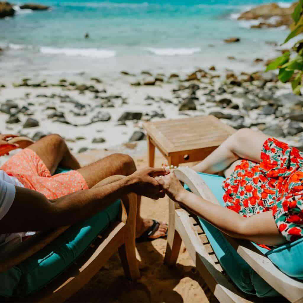 A couple in sitting along a beautiful beach view, holding each other's hands, after reading these 10 tips for a happy marriage