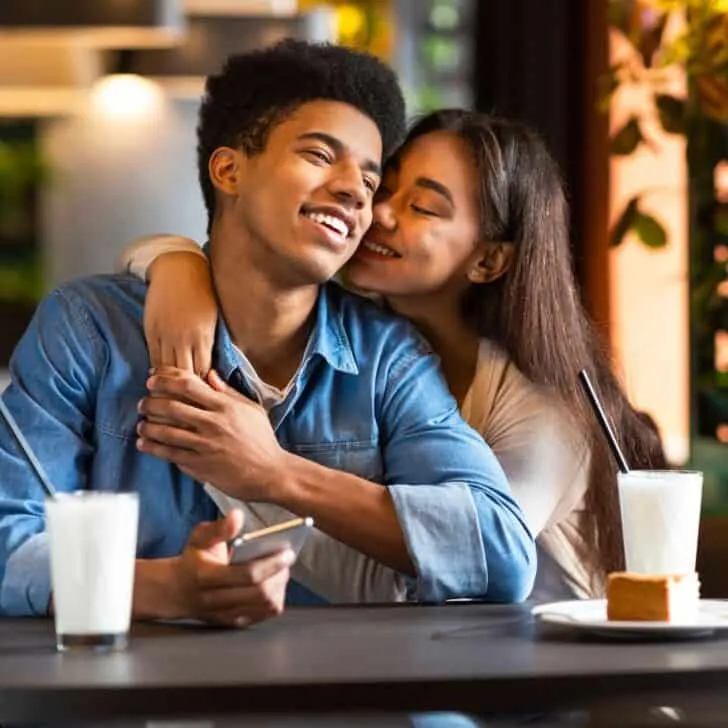 A teen couple at a restaurant, the girl leaning in the boy's cheeks, after reading these fall date ideas for teens