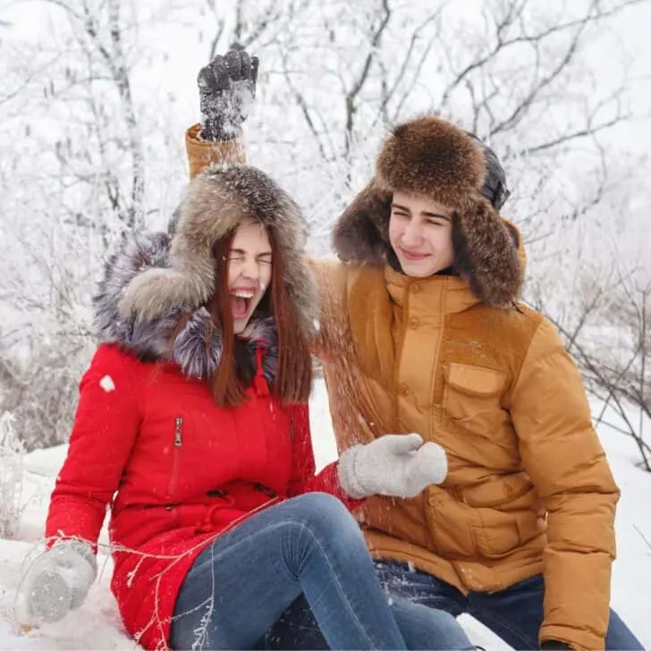 A teen couple in the snow, the boy spreading some snow at the girl's head, after reading these winter date ideas for teenage couples