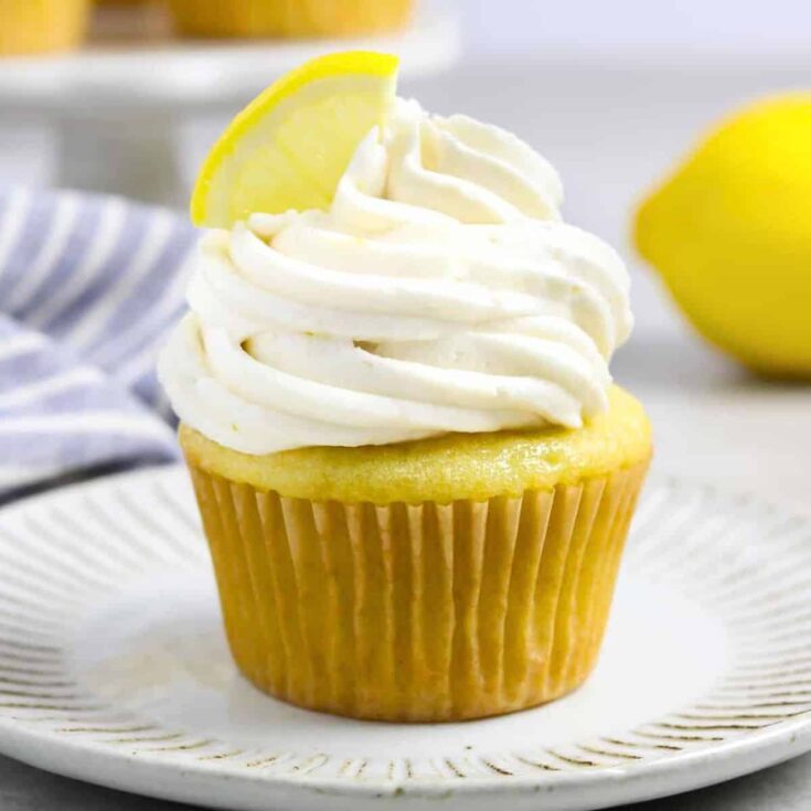 Vegan lemon cupcake topped with white icing and a slice of lemon, baked after reading these Easter cupcakes