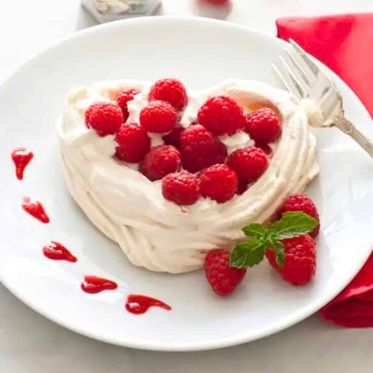 A plate of meringue hearts with whipped cream and raspberries made after reading these Valentines Day Desserts