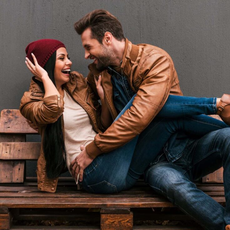 A couple sitting on a bench, laughing at a bet they made together, after reading these fun bets for couples