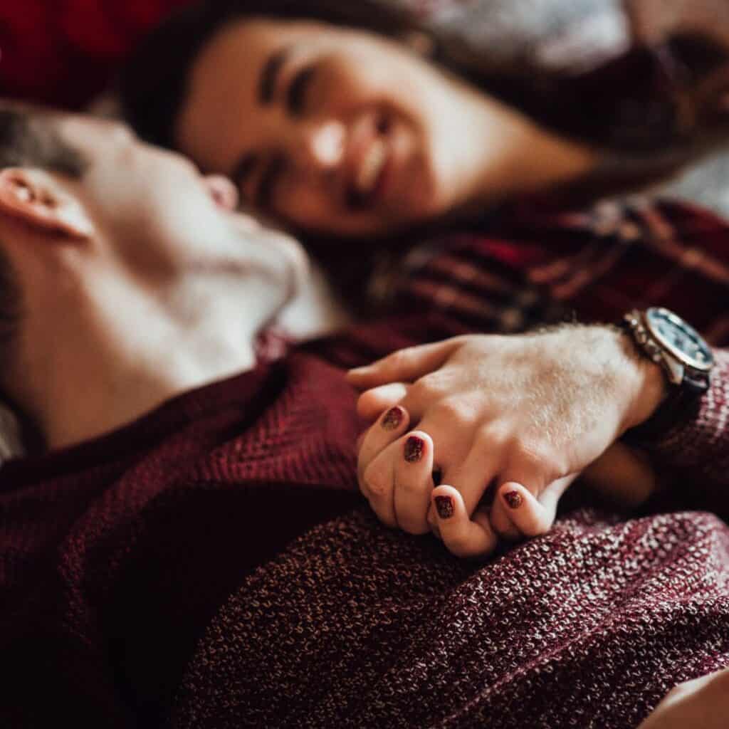 A couple holding hands as they lay down in bed: How to survive your family Christmas