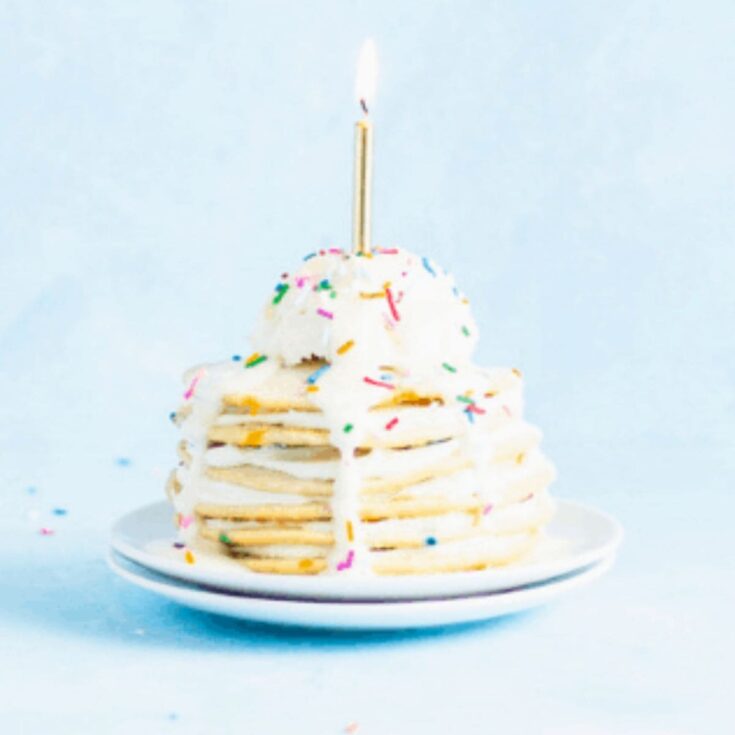 A stack of birthday cake pancakes topped with a candle