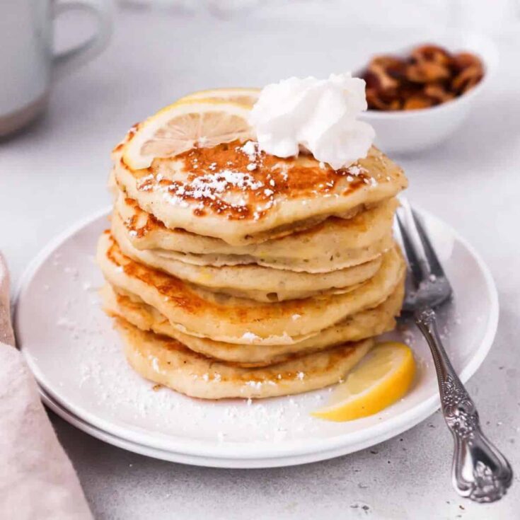 Buttermilk lemon pancakes topped with whipped cream and sliced lemon