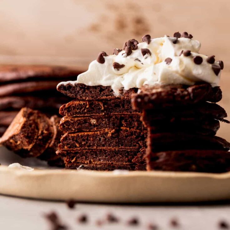 A plate of sliced chocolate pancakes topped with whipped cream and chocolate chips