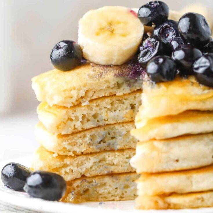 Sliced fluffy oat milk pancakes topped with sliced bananas and blueberries