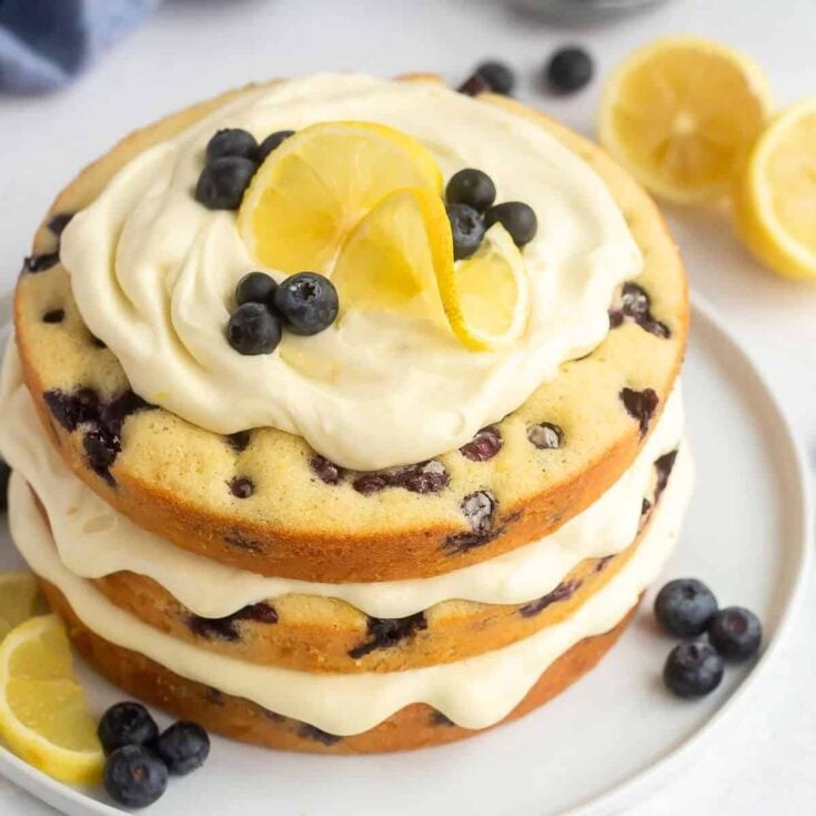 Lemon blueberry cake topped with cream, slice of lemon, and blueberries
