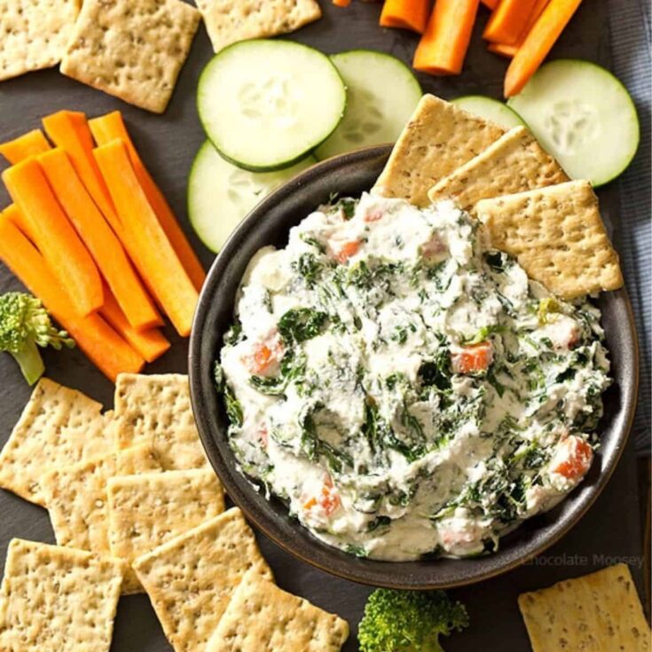 A bowl of Spinach ranch dip with biscuits, carrots, and cucumbers on the side