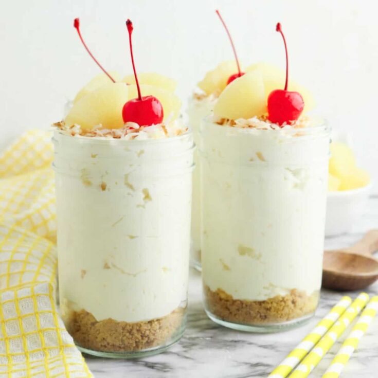 Two Pina colada cheesecake jars topped with pineapple slices and cherry